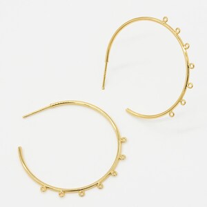 May include: Gold hoop earrings with multiple small loops hanging from the bottom of the hoop.