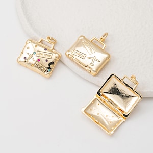 Puede incluir: Tres abalorios de maleta de color dorado con apertura con bisagra. Un abalorio tiene un diseño de avión y el texto "NEW YORK" y "LONDON". Otro abalorio tiene el texto "LONDON" y "NEW YORK". El tercer abalorio está abierto y muestra el interior de la maleta.