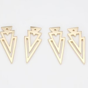 May include: Four gold-colored, geometric arrow-shaped jewelry components. Each component features a layered design with a small hole at the top for attachment. The components are arranged on a white surface.