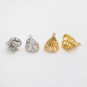 May include: Four filigree metal bead caps in silver and gold tones. Two are silver, and two are gold. The bead caps have an openwork design with a loop at the top for stringing.
