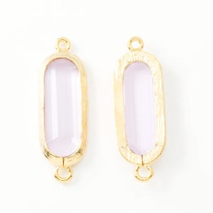Puede incluir: Dos conectores de joyería rectangulares dorados con un centro lila claro. Cada conector tiene un lazo en la parte superior e inferior para sujetar a otros componentes de joyería. Los conectores se muestran sobre un fondo blanco.