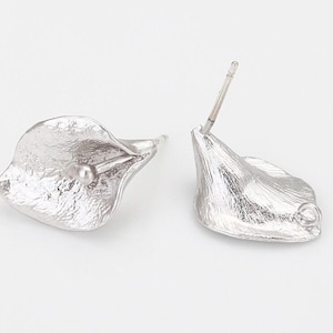 Puede incluir: Un par de pendientes de plata con forma de cala. Cada pendiente tiene una superficie texturizada y un pequeño adorno en forma de perla en el centro. Los pendientes se muestran sobre un fondo blanco.