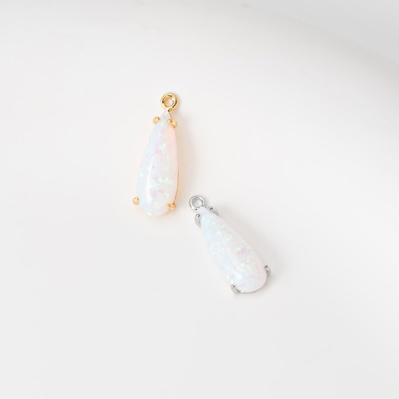 May include: Two teardrop-shaped pendants featuring iridescent white opal-like stones. One pendant is set in a gold-toned metal frame with a small circular bail at the top, while the other is set in a silver-toned metal frame with a matching bail.