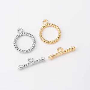 May include: Two silver and two gold twisted metal clasps for jewelry making. The clasps are in the shape of a circle and a bar.
