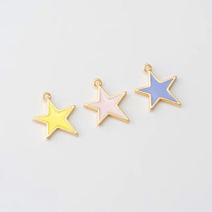 May include: Three star-shaped charms in yellow, pink, and light blue with gold-colored borders. Each charm has a small loop at the top for attaching to jewelry or other crafts. The charms are set against a white background.