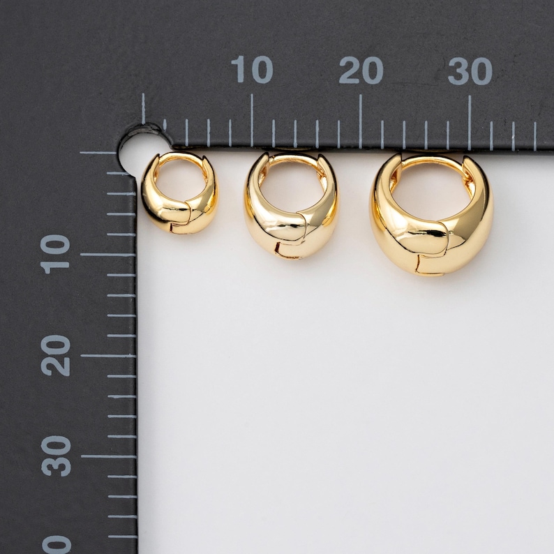 May include: Three gold-coloured hoop earrings in different sizes. The earrings have a shiny, rounded design. The smallest earring is about 1 cm in diameter, the middle one is 1.5 cm, and the largest is 2 cm.