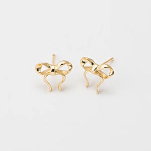 Op de afbeelding: Een paar gouden oorbel studs in de vorm van een strik.