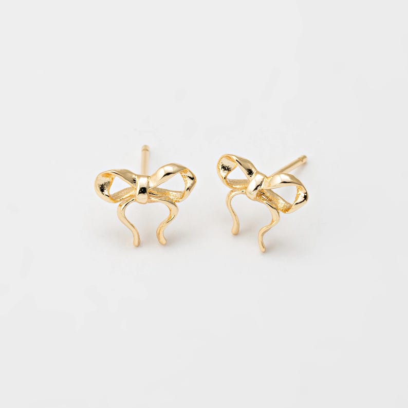 Op de afbeelding: Een paar gouden oorbel studs in de vorm van een strik.