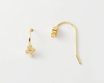 May include: A pair of gold-colored earrings with a delicate design. Each earring features a small cluster of three clear, round gemstones. The earrings have a simple, elegant hook design, perfect for everyday wear.
