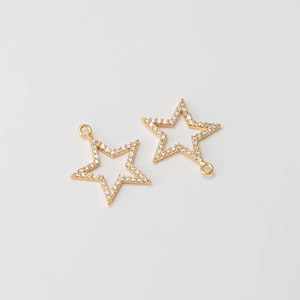 May include: Two gold-colored star-shaped charms with clear, sparkling stones. Each charm has a loop at the top for hanging. The stars are set against a plain white background.