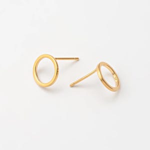 May include: A pair of gold-colored circle stud earrings. Each earring features a simple, open circle design attached to a post for pierced ears. The earrings are set against a plain white background.