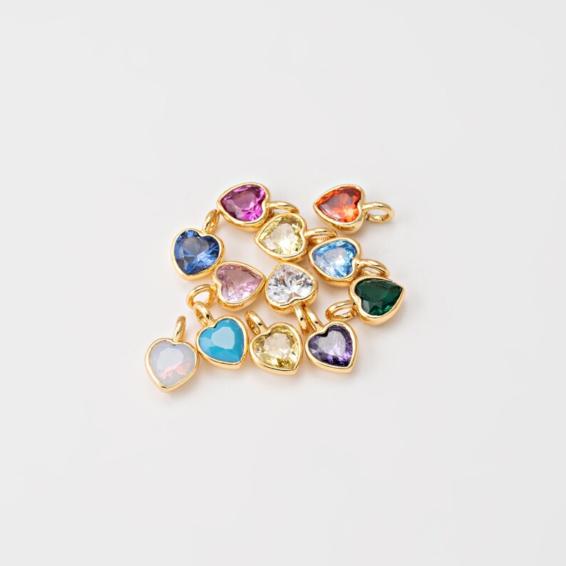 May include: A collection of gold heart-shaped charms with various colored gemstones, including turquoise, pink, red, blue, green, and clear.