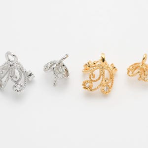May include: Four ornate jewelry findings in silver and gold tones. Two are silver, featuring a filigree design with clear gemstones. The other two are gold, with a similar filigree pattern and clear gemstones. These findings are likely for jewelry making.