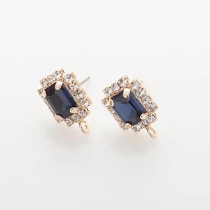 Könnte beinhalten: Ein Paar goldfarbene Ohrstecker. Jeder Ohrring hat einen rechteckigen, dunkelblauen Edelstein, der von einem quadratischen Rahmen aus kleinen, klaren Kristallen umgeben ist. Am unteren Ende jedes Ohrrings ist eine kleine Schlaufe angebracht.