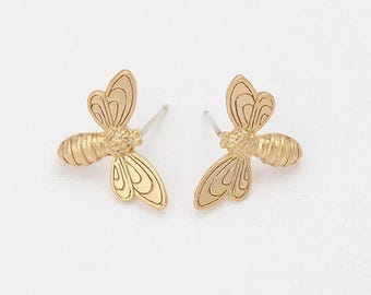 May include: A pair of gold-colored bee stud earrings. Each earring features a detailed bee design with wings and a textured body. The earrings are set against a white background.