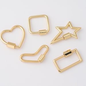 Könnte beinhalten: Fünf goldfarbene Karabinerverschlüsse in verschiedenen Formen: ein Herz, ein Quadrat, ein Stern, eine gebogene Form und ein Rechteck. Jeder Verschluss hat einen Schraubverschlussmechanismus. Die Verschlüsse werden auf weißem Hintergrund gezeigt.