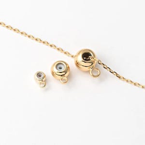 May include: Close-up of gold-coloured jewellery components, including a chain and three round clasps. The clasps have a small loop for attachment and a hollow centre. The chain and clasps are on a white background.