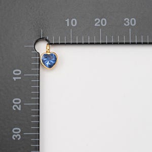 May include: A gold heart-shaped charm with a blue gemstone in the center.