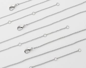 May include: A set of six silver chain extenders, each with a lobster clasp on one end and a jump ring on the other. The extenders are arranged in a row, with the longest extender at the top and the shortest extender at the bottom.