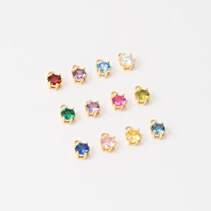 May include: Assortment of 12 gold-tone charm pendants with various colored round gemstones. Each pendant features a prong setting.