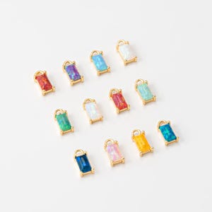 May include: Assortment of 12 gold-toned charms with rectangular opal-like stones in various colors, including blue, green, red, pink, white, and yellow.