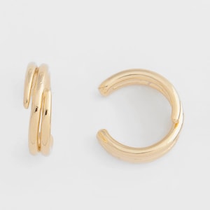 May include: A pair of gold ear cuffs. One cuff is a single, thick band, while the other is a double band that wraps around the ear.