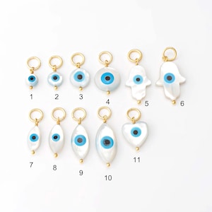 May include: A collection of eleven gold-toned charms with white, blue, and gold accents. The charms feature various shapes, including round, oval, and hand-shaped designs, each with a blue eye motif. The charms are ideal for jewelry making.