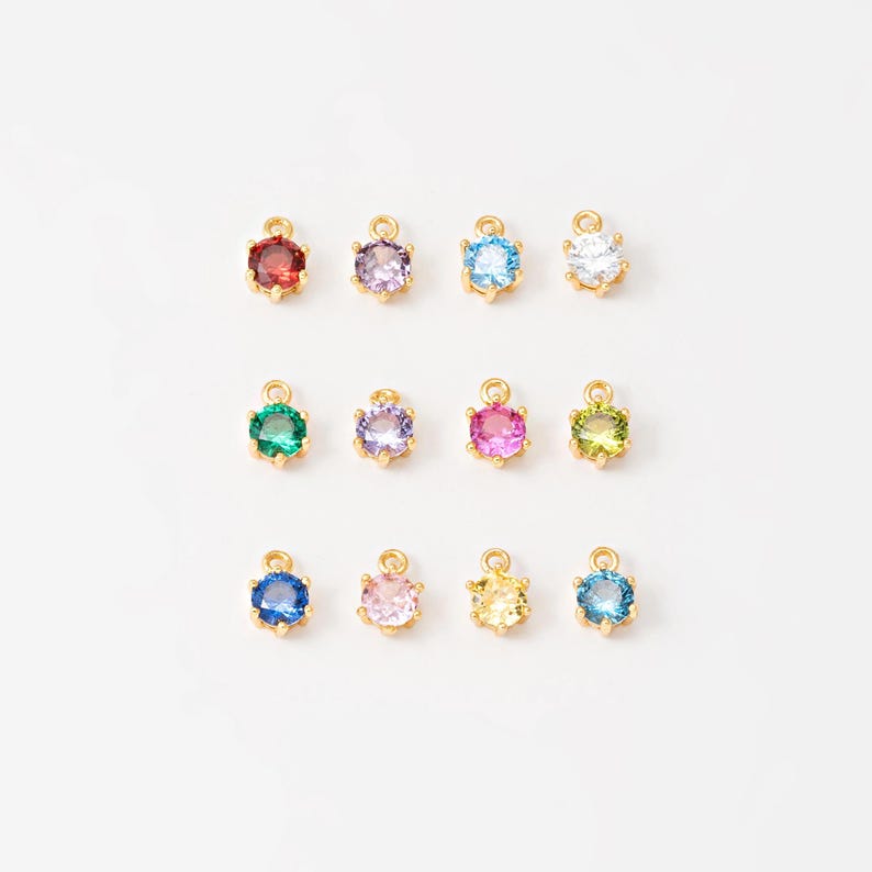 May include: Assortment of 12 gold-tone charms with round, faceted gemstones in various colors, including red, purple, blue, green, pink, and clear.