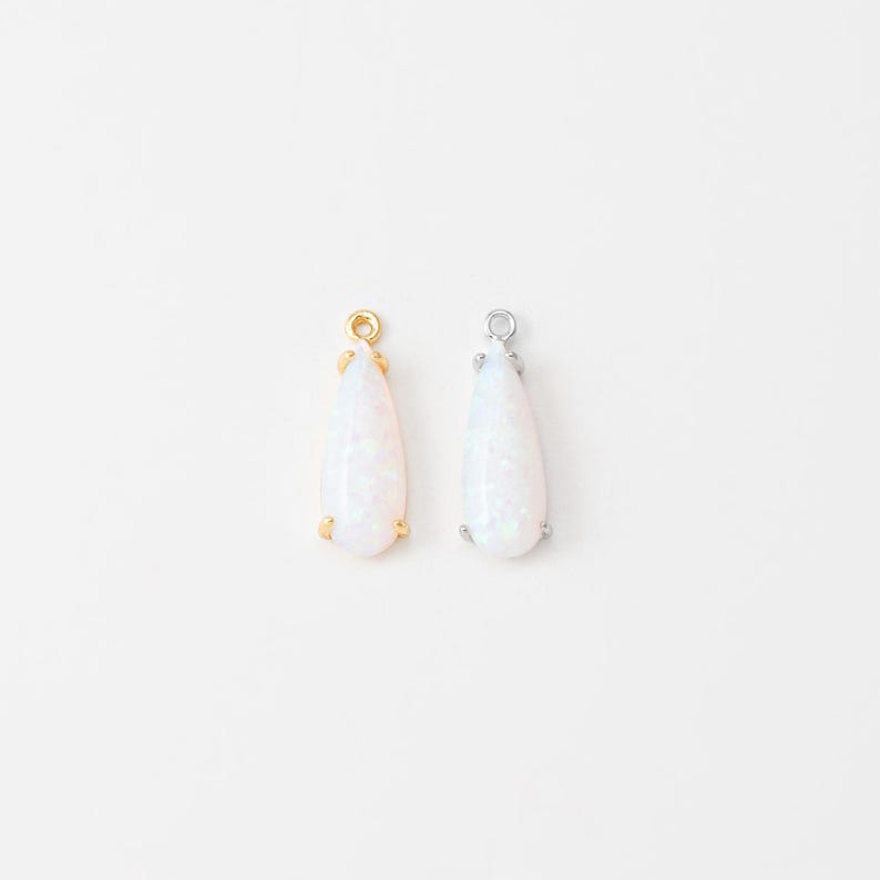 May include: Two teardrop-shaped pendants featuring iridescent white stones. One pendant is set in a gold-toned metal frame with a small loop at the top, and the other is set in a silver-toned metal frame with a matching loop at the top.