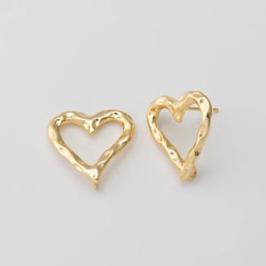 May include: A pair of gold-colored heart-shaped earrings. The earrings have a textured, hammered appearance and a post backing. The open heart design is visible against a white background.