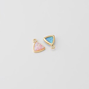 May include: Two gold triangle charms with opal stones. The charm on the left has a pink opal stone and the charm on the right has a blue opal stone.