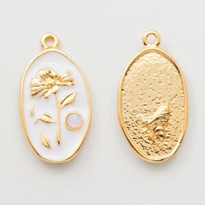 Peut inclure: Deux breloques ovales en or. Un charme présente un fond en émail blanc avec une fleur dorée et une petite pierre d'opale. L'autre charme présente un motif d'abeille dorée.