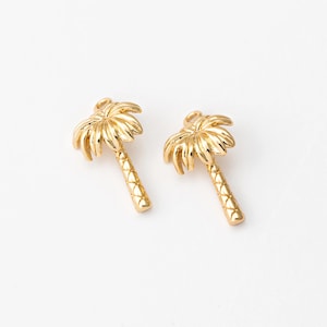 May include: Two gold-colored palm tree stud earrings. The earrings feature detailed palm fronds and textured trunks. The earrings are set against a white background, highlighting their tropical design.