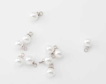 May include: Several white faux pearl beads with silver loops are scattered on a white background. The beads are round and shiny, perfect for crafting jewellery. Each bead has a small loop attached.