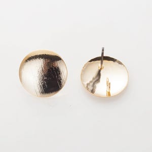 May include: Two gold-colored, round stud earrings. Each earring has a brushed metal texture on the front and a post for piercing. The earrings are set against a white background. The earrings are a simple, elegant design.