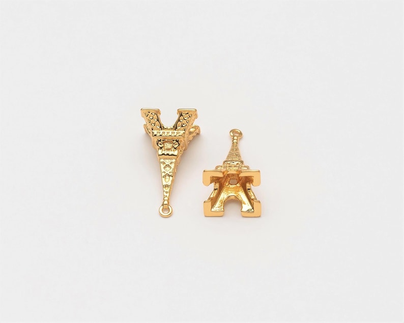 May include: Two gold-coloured Eiffel Tower charms. One charm has a loop at the top and the other has a loop at the bottom.
