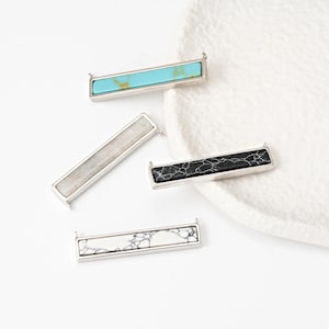 May include: Four silver bar pendants with different colored stone inlays. The stones are turquoise, white, black, and gray.