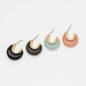 May include: Four pairs of hoop earrings in a row. Each earring has a gold-colored curved metal accent. The hoops are in black, brown, light blue, and peach colors. The earrings are on a white background.