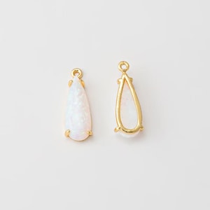 May include: Two teardrop-shaped jewelry charms featuring a gold-toned metal frame and a smooth, iridescent white stone inlay. Each charm includes a small circular loop at the top for attachment, showcasing a polished finish and a classic design.