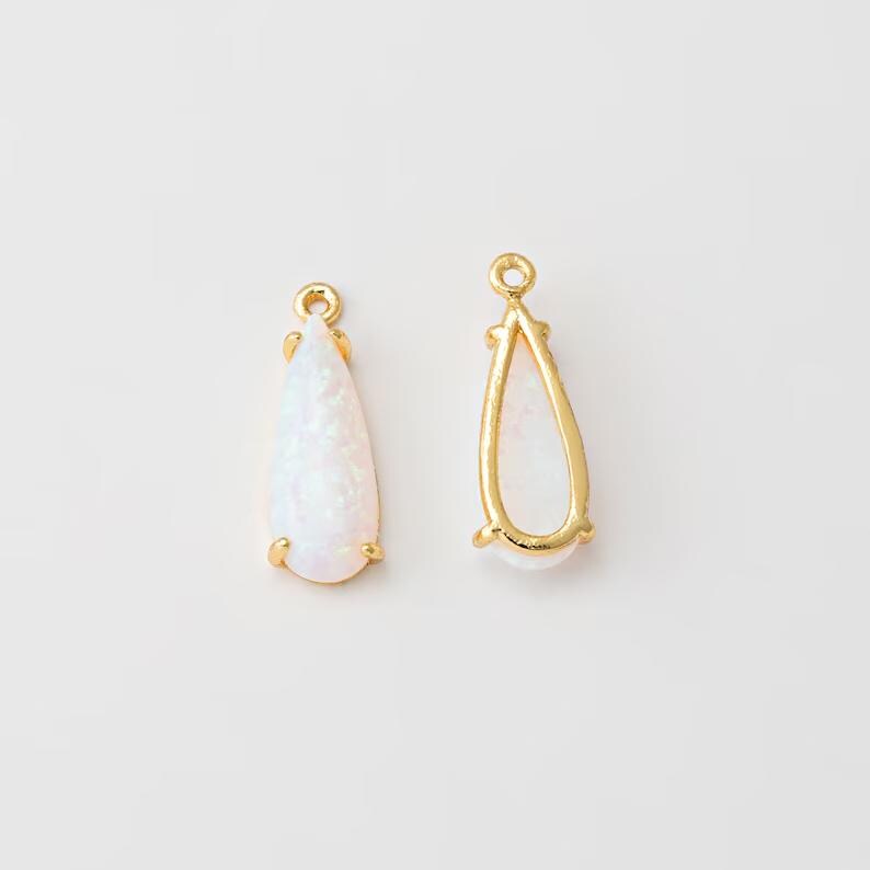 May include: Two teardrop-shaped jewelry charms featuring a gold-toned metal frame and a smooth, iridescent white stone inlay. Each charm includes a small circular loop at the top for attachment, showcasing a polished finish and a classic design.