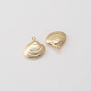 May include: Two gold-colored seashell charms with a textured, ridged surface. Each charm has a small loop at the top for attaching to jewelry. The charms are on a white background.