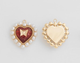 Puede incluir: Dos dijes de corazón de oro, uno con un diseño de mariposa de esmalte rojo rodeado de perlas blancas, y el otro con un diseño de corazón de oro liso.