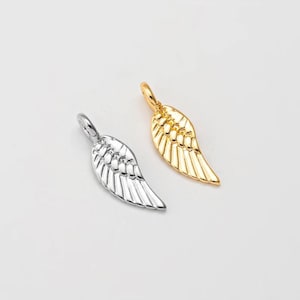 May include: Two wing-shaped pendants, one silver-colored and the other gold-colored, are displayed against a white background. Each pendant has a loop at the top for attaching to a chain or other jewelry component.