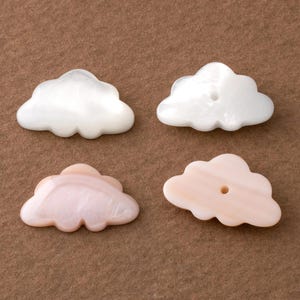 Op de afbeelding: Vier wolk-vormige kralen. Twee zijn wit en twee zijn lichtroze. Elke kraal heeft een gat erdoorheen. De kralen hebben een parelmoerglans en zijn waarschijnlijk gemaakt van parelmoer.