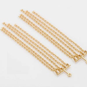 May include: Two gold-coloured chain connectors, each with three strands of delicate chains. Each connector has a T-shaped bar with a small loop at the end. The chains are arranged in parallel lines.