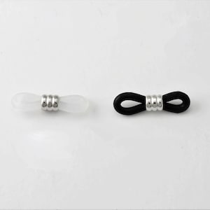 以下が含まれることがあります： 2つの眼鏡リテーナー。1つはシルバーのアクセントが付いた白、もう1つはシルバーのアクセントが付いた黒です。リテーナーは眼鏡を所定の位置に保持するように設計されています。背景は白です。