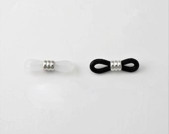 May include: Two eyeglass retainers. One is white with a silver accent, and the other is black with a silver accent. The retainers are designed to hold eyeglasses in place. The background is white.