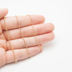 Op de afbeelding: Drie delicate goudkleurige kettingen met verschillende kettingstijlen. Eén ketting heeft kleine, gelijkmatig verdeelde kralen, de andere hebben een klassiek schakelontwerp. De sieraden worden getoond tegen een effen witte achtergrond.