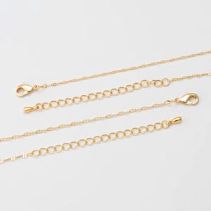 Puede incluir: Primer plano de cadenas y extensores de joyería doradas. Las cadenas tienen patrones delicados y repetitivos, y los extensores presentan pequeños anillos conectados. Cada cadena tiene un cierre de langosta para una sujeción segura.