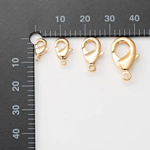 May include: Three gold-toned lobster clasps of different sizes, measured in inches on a black ruler.